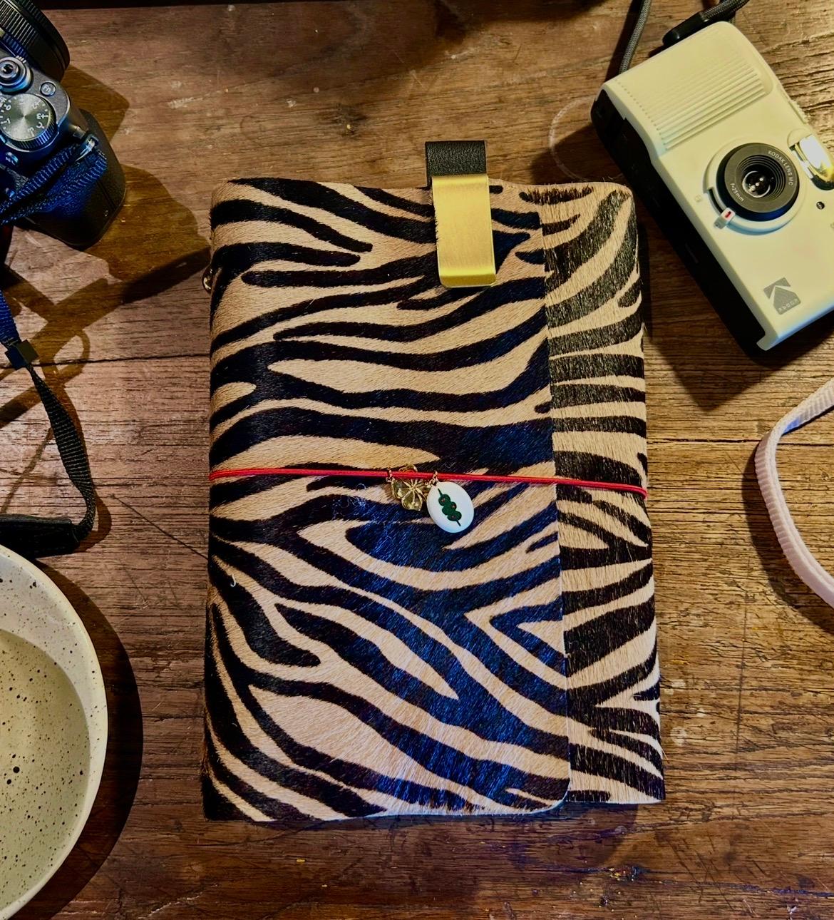A zebra-print leather journal on a wooden table beside a vintage camera
